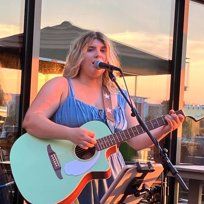 Girl with blonde hair playing a light green guitar outside at sunset