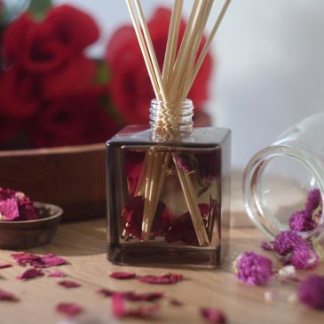A reed diffuser with dried flowers and scattered petals on a wooden surface.
