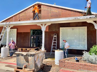 Workers renovating the exterior of a brown house under a clear sky.