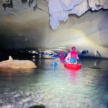 Kayakers exploring a large underground cave with calm water.