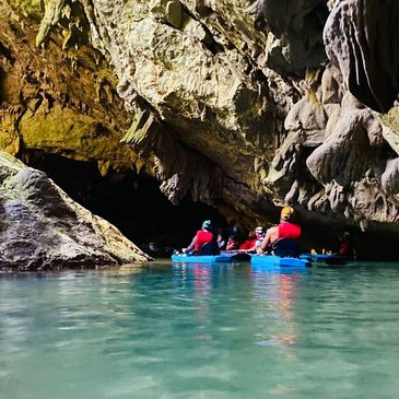 Group kayaking into a cave with rocky walls and clear water.