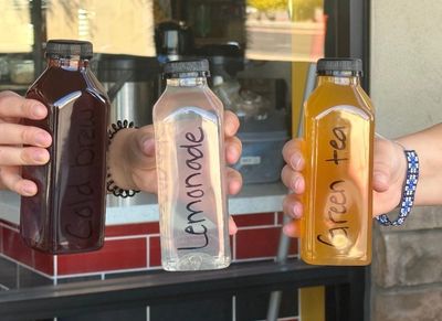 Three hands holding bottles of cold brew, lemonade, and green tea.
