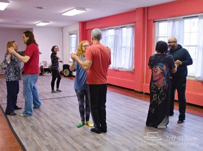 People practicing partner dance in a bright studio with coral walls.