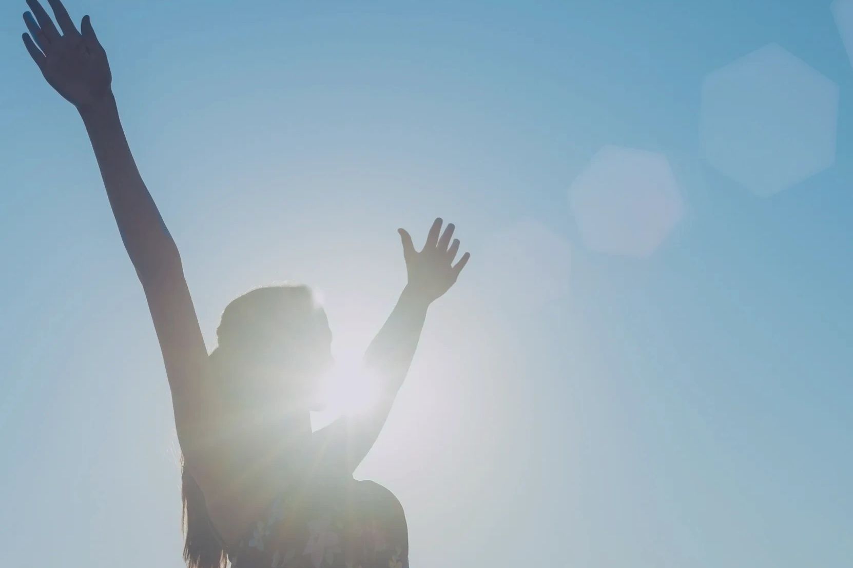 Woman silhouetted against a blue sky with arms in the air