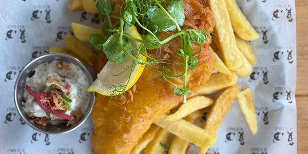 Crispy fish and chips with tartar sauce and lemon wedge.
