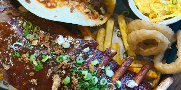 A delicious plate with ribs, fries, onion rings, and a side of macaroni salad.