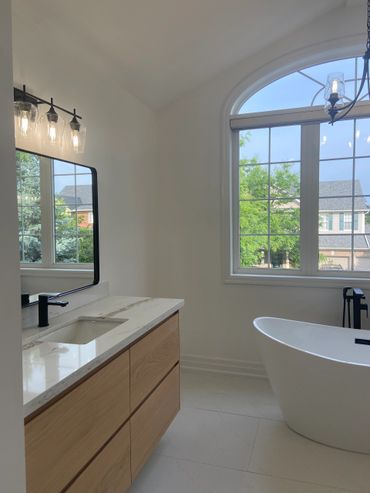 Modern bathroom with a freestanding tub and wooden vanity under large arched window.