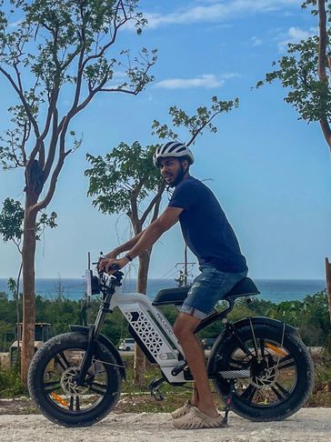 Man posing on an electric bike near trees and ocean.