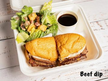 Beef dip sandwich with salad and dipping sauce in a takeout container.