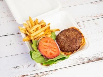 Takeout burger with lettuce, tomato, and fries in a white container.
