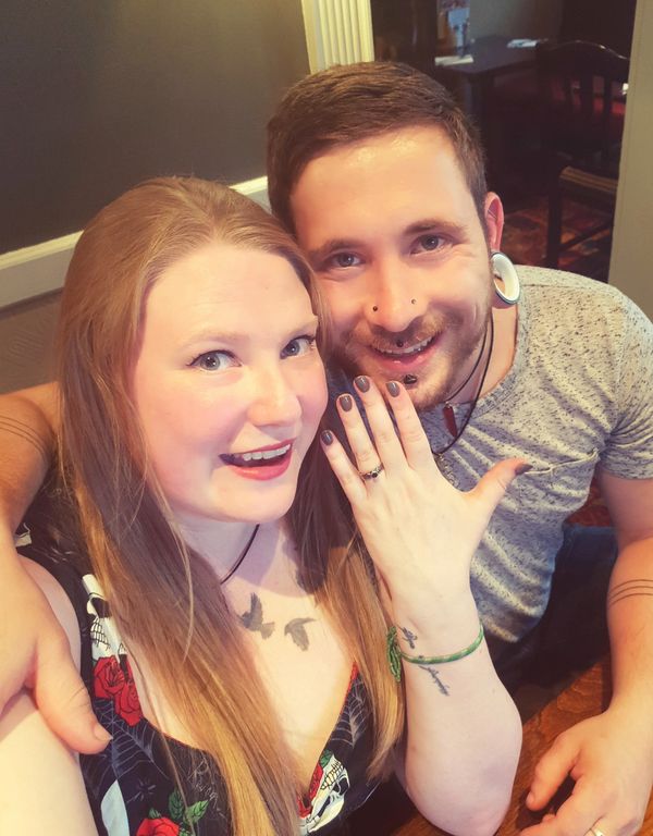 Pete with his arm round wife as she shows off engagement ring to camera, both smiling