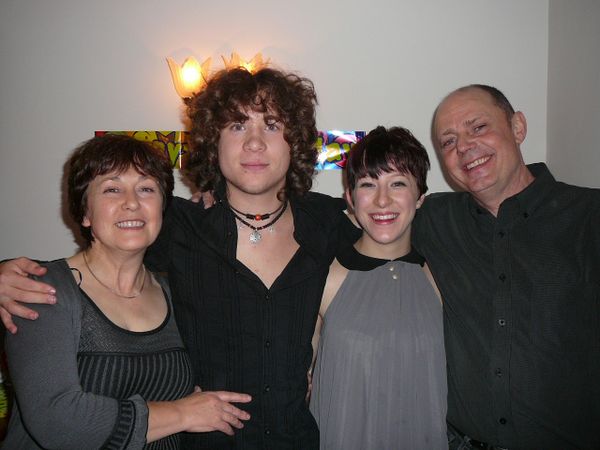 Pete with curly hair smiling with his sister and parents at camera, all wearing black and grey