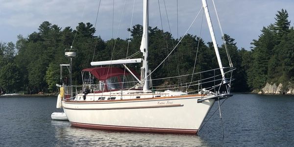 A sailboat named Enter Now anchored on calm water near a forested shore.