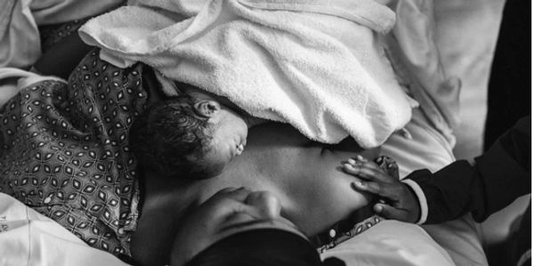 Newborn baby resting on mother's chest wrapped in a towel after birth.