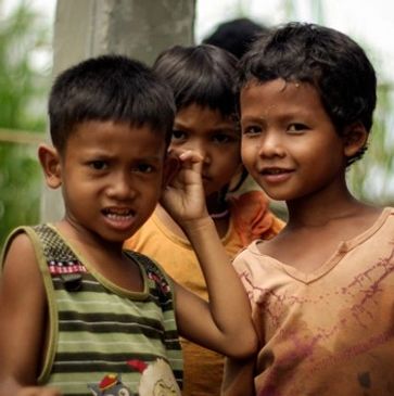 Three children standing close together outdoors, looking at the camera.