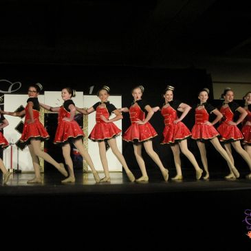 Line of dancers in red costumes performing on stage.