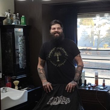 Bearded man with tattoos smiling in a barbershop.