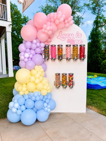 Colorful candy dispenser with pastel balloons for a first birthday.