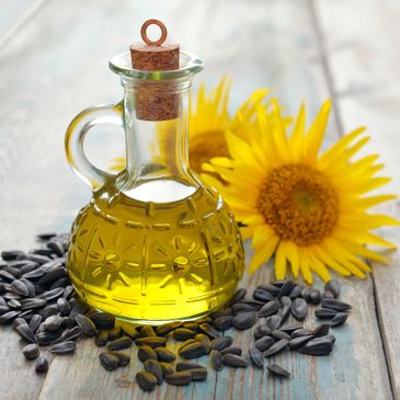 A glass bottle of sunflower oil surrounded by sunflower seeds and bright yellow flowers.