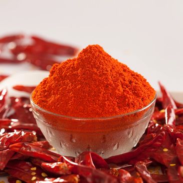 A bowl of bright red chili powder surrounded by dried red chilies.