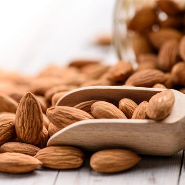 Close-up of almonds with a wooden scoop and a glass jar in the background.