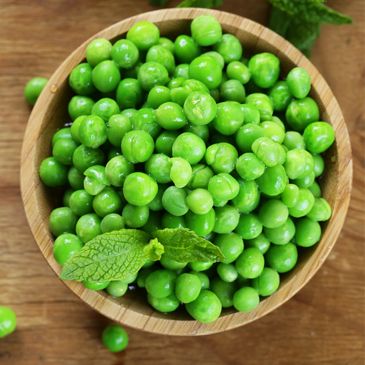 Fresh green peas in a wooden bowl with a mint leaf.