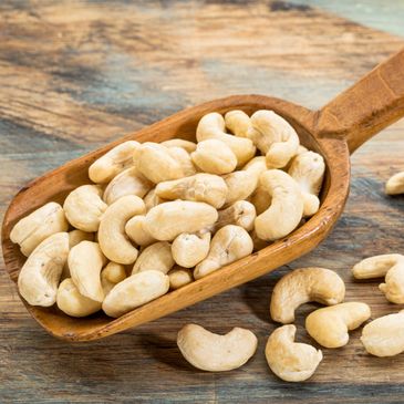 Raw cashew nuts in a wooden scoop on a rustic surface.