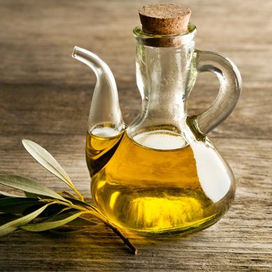 Glass bottle of olive oil with olive branch on wooden surface.