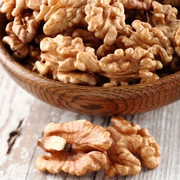 Close-up of shelled walnuts in a wooden bowl on a rustic surface.