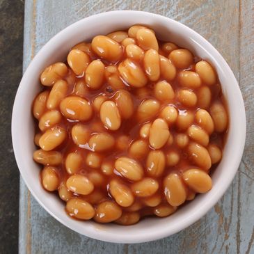 A bowl of baked beans in tomato sauce on a wooden surface.