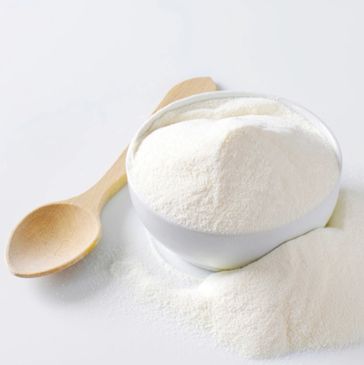 A bowl and spoon with white powder on a white surface.
