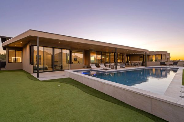 Modern home with large glass windows and a pool at sunset.