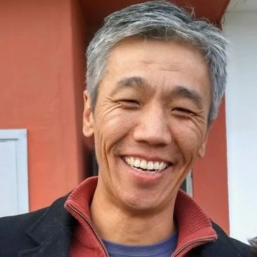 Smiling man with gray hair wearing a black jacket and red collar.