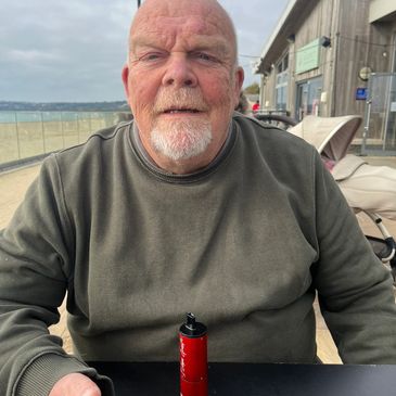 Older man sitting at an outdoor table with a red vape device.