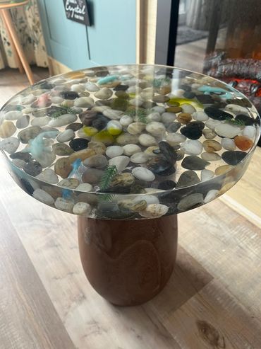 Round table with a clear top filled with colorful pebbles and a brown base.
