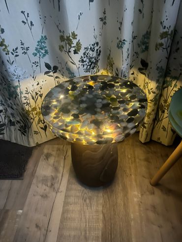 Illuminated decorative table with leaf patterns beside floral curtains.