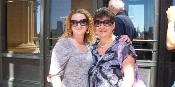 Two women posing outdoors, smiling with sunglasses on.