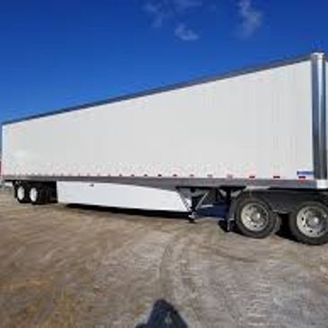 White semi-trailer truck parked on gravel under blue sky.