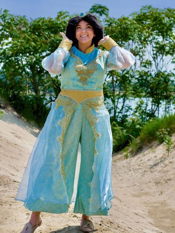 Personnage royal en costume turquoise et doré, souriant sur une dune ensoleillée.