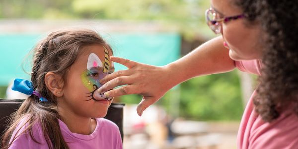 Maquillage licorne coloré en cours lors d’une fête d’enfants en plein air.