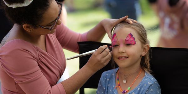 Maquillage papillon rose en cours lors d'une animation pour enfants à l’extérieur.