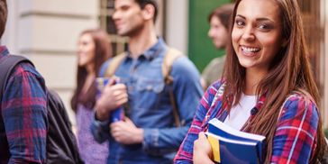 Smiling student holding books with peers in the background.