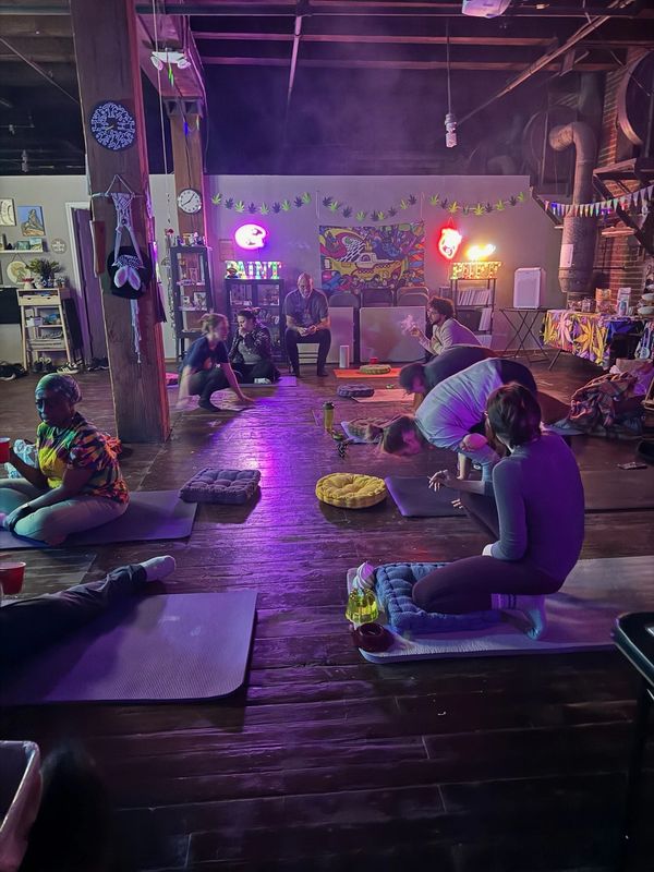 People gathered in a dimly lit room with colorful lights, sitting on mats and cushions.