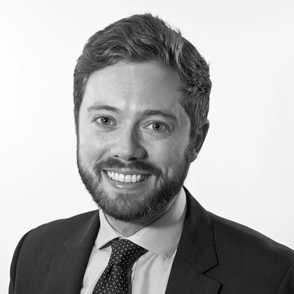 Smiling man in suit and tie posing against a plain background.