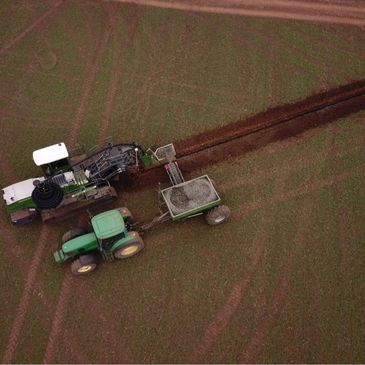 Aerial image of drainage trencher working with gravel cart and tractor.