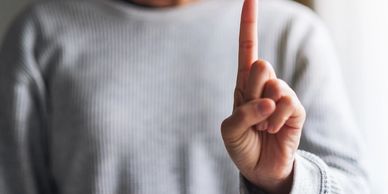 A close-up image of a woman holding one finger up to the viewer.  The image of the woman is blurred  