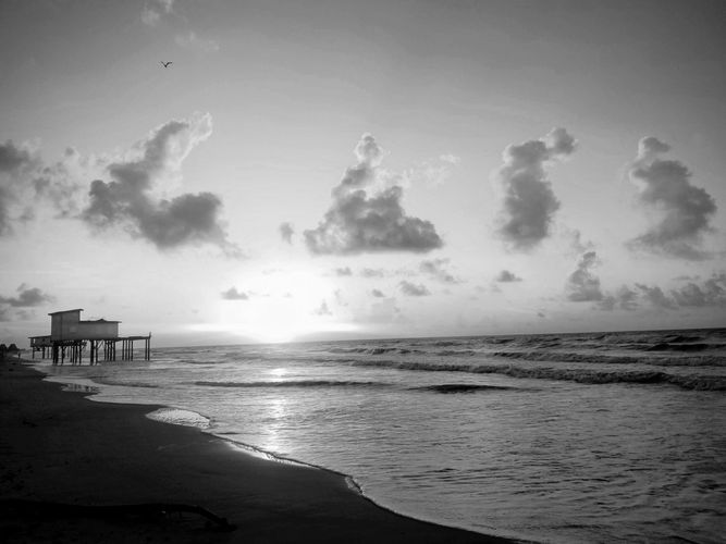 Sunset over ocean with silhouetted pier and glowing clouds.