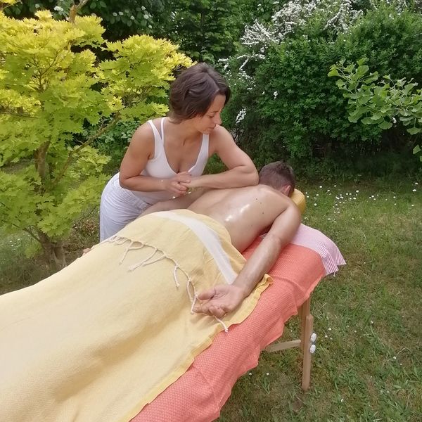 A woman gives a relaxing outdoor massage to a man on a massage table.
