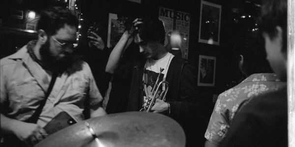 Black and white photo of musicians preparing to play in a dimly lit room.