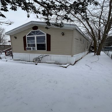 A mobile home surrounded by snow and bare trees in winter.